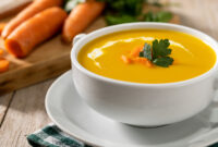 Carrot soup with cream and parsley on wooden table.